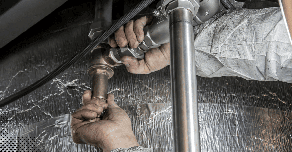 Hands tightening metal plumbing pipes under a sink.