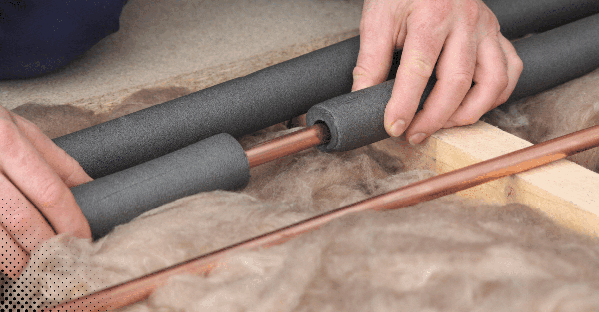 Hands installing foam insulation around copper pipes.