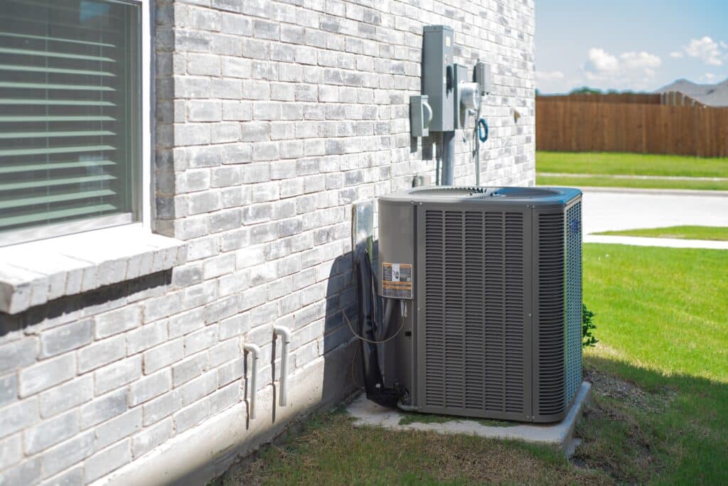 Residential HVAC air conditioning condenser unit at exterior brick wall inspected during a home inspection in Fort Worth, TX